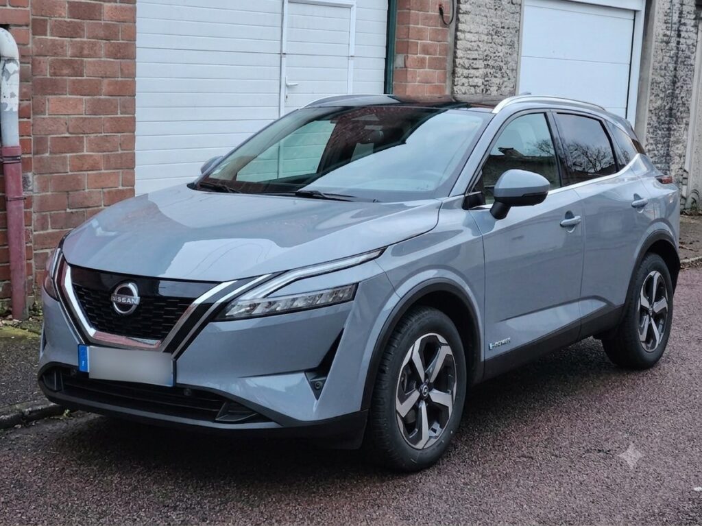 Nissan Qashqai e-power gris stationné devant un garage en briques, vue de trois-quarts avant