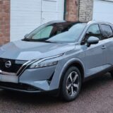 Nissan Qashqai e-power gris stationné devant un garage en briques, vue de trois-quarts avant