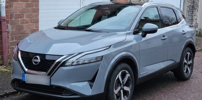 Nissan Qashqai e-power gris stationné devant un garage en briques, vue de trois-quarts avant